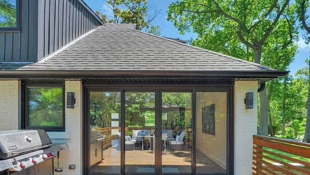 Ett modernt hus med en veranda, en grill och en uteplats med utemöbler.