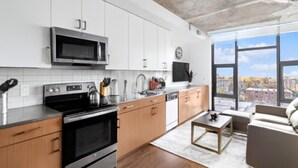 Une cuisine moderne avec des armoires blanches, un four à micro-ondes, une cuisinière et un lave-vaisselle. Une grande fenêtre offre une vue sur la ville.
