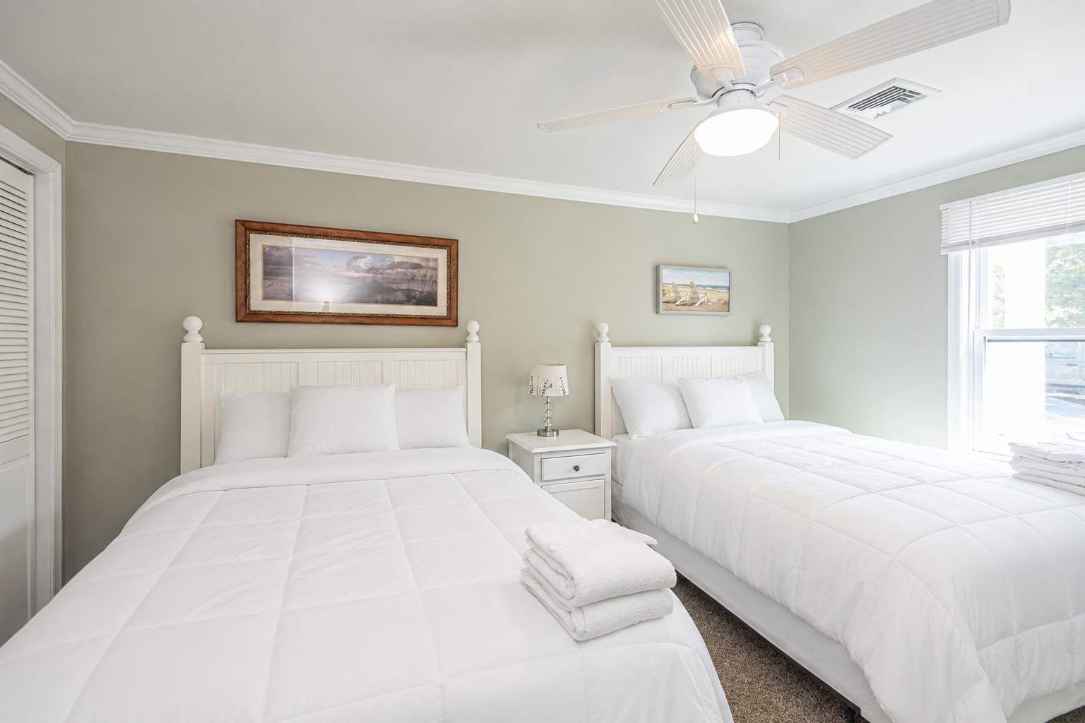 A bedroom with two beds, a ceiling fan, and artwork on the walls.