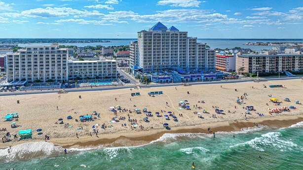 Ein Strandhotel mit mehreren Gebäuden, einem Sandstrand und Meereswellen.