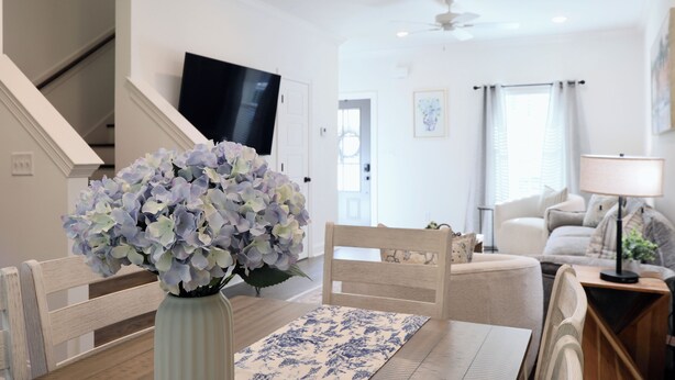 Ein Wohnzimmer mit einem Holzesstisch, einem Blumenstrauß, einer Couch, einem Fernseher und einer Treppe.