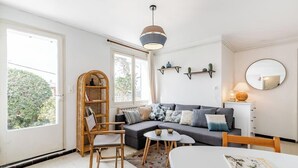 En moderne stue med sofa, spisebord, bogreol og et stort vindue.