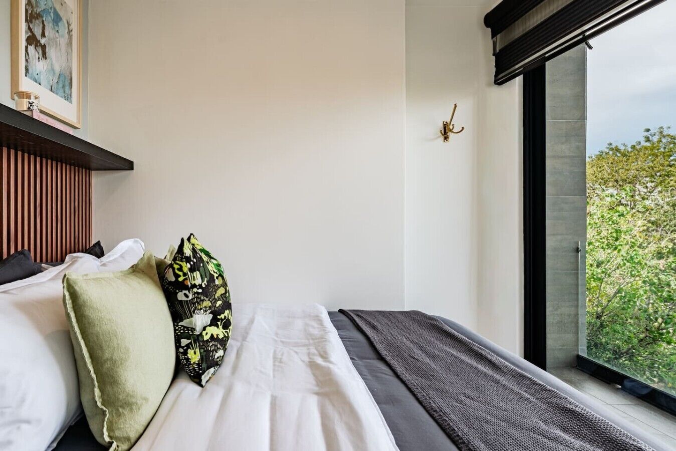 A modern hotel room with a large window, a bed with white linens, and a wooden headboard.