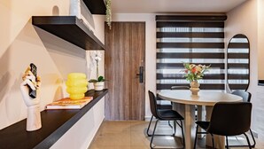 Un comedor moderno con una mesa redonda, sillas negras, una puerta de madera y un estante negro con objetos decorativos.