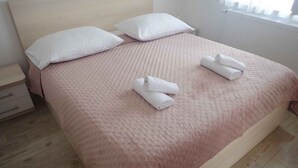 En snyggt bäddad säng med ett rosa täcke, två kuddar och två hoprullade handdukar.