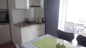 Una cucina moderna con mobili bianchi, un lavello e un piano cottura. C'è un'area pranzo con tavolo e sedie, e vista sull'esterno attraverso ampie finestre.