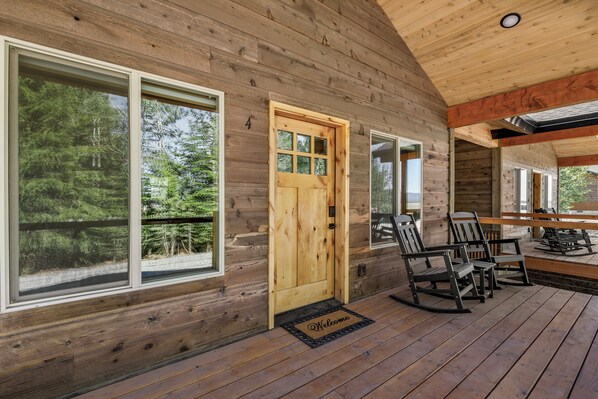 A wooden cabin with large windows, a wooden door, and a porch with chairs.