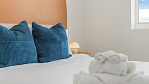Un lit bien fait, avec des oreillers bleus et une serviette blanche.