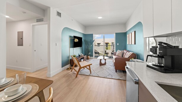 Un appartement moderne comprenant un coin repas, un salon avec un canapé et une table basse, une cuisine équipée d’une machine à café et un balcon avec vue.