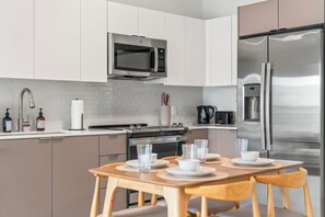 A modern kitchen with stainless steel appliances, a dining table set with plates and glasses, and a water dispenser. - 2BR Luxury King Suites + Parking Clean and New (Hallandale Beach)