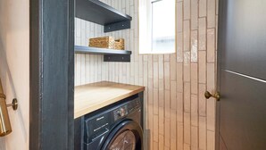 A compact laundry room with a washing machine, wooden shelves, and a window. - Host Stay - Hecklers Nook (Barnard Castle)