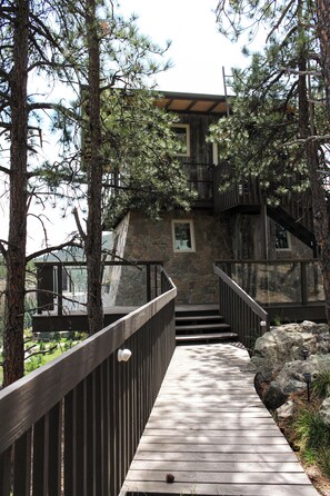 Eine Holztreppe führt zu einem von Bäumen umgebenen Steinhaus.