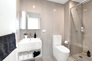 A modern bathroom with a white sink, mirror, toilet, and glass shower enclosure. - Incredible Views - Bright & Spacious CBD Escape (Melbourne)