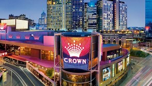 Un hotel de varios pisos con un llamativo letrero 'Crown', rodeado de edificios altos y una calle concurrida.