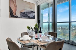 A dining area with a glass table, white plates, and wine bottles, overlooking a cityscape. - Incredible Views - Bright & Spacious CBD Escape (Melbourne)