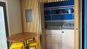 A compact kitchen with a wooden wall panel, a built-in stove, and a shelf with kitchen items.