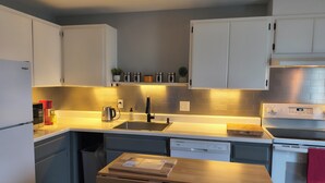 A modern kitchen with white cabinets, a stainless steel backsplash, a built-in dishwasher, and a wooden countertop.