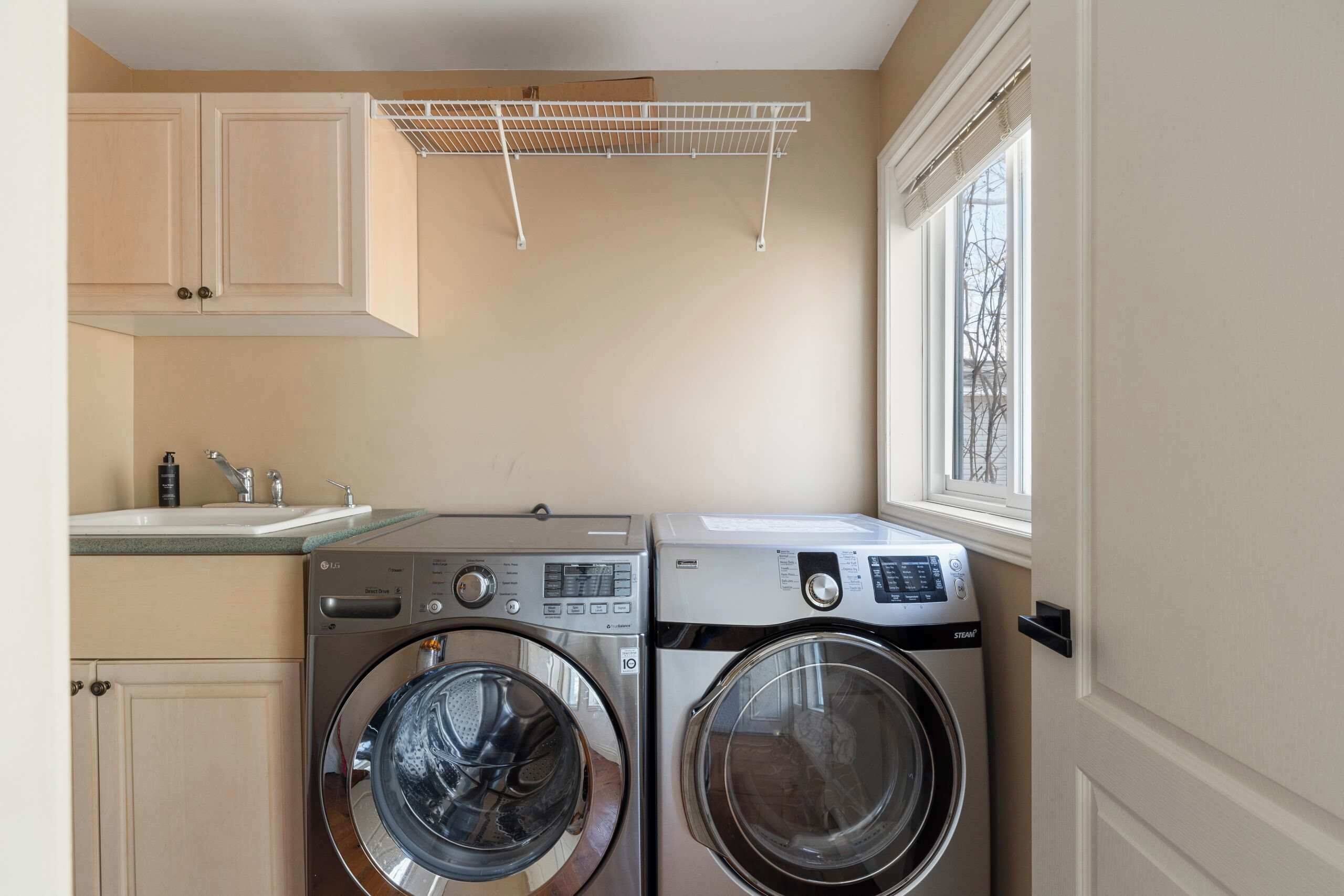 A laundry area with two washing machines, a drying rack, a sink, and cabinets.