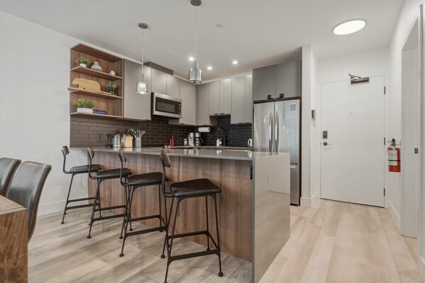 A modern kitchen with a central island, bar stools, and a refrigerator.