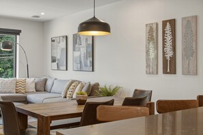 A modern living room with a sofa, dining table, and chairs. There are abstract paintings on the wall and a potted plant on the table.
