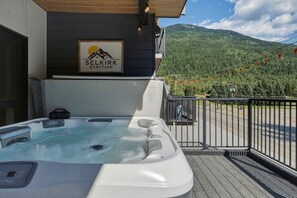 A hot tub on a balcony with a mountain view, a sign for 'Selkirk Staytion,' and a railing.
