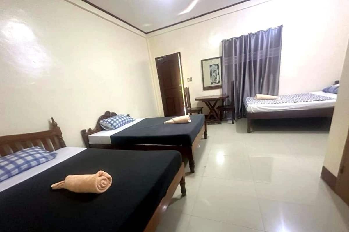 A hotel room with two beds, a small table, a chair, and a door.