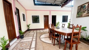 A spacious dining area with a round wooden table and chairs, surrounded by potted plants and a patterned floor. - La Petite Pension (Puerto Princesa)