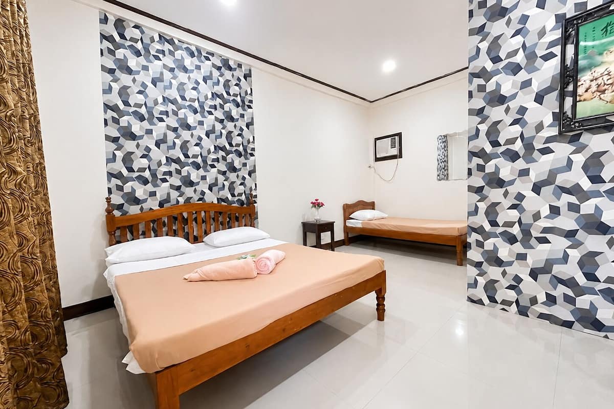 A hotel room with two beds, a wooden headboard, a small bedside table with a vase, and a wall-mounted air conditioning unit.