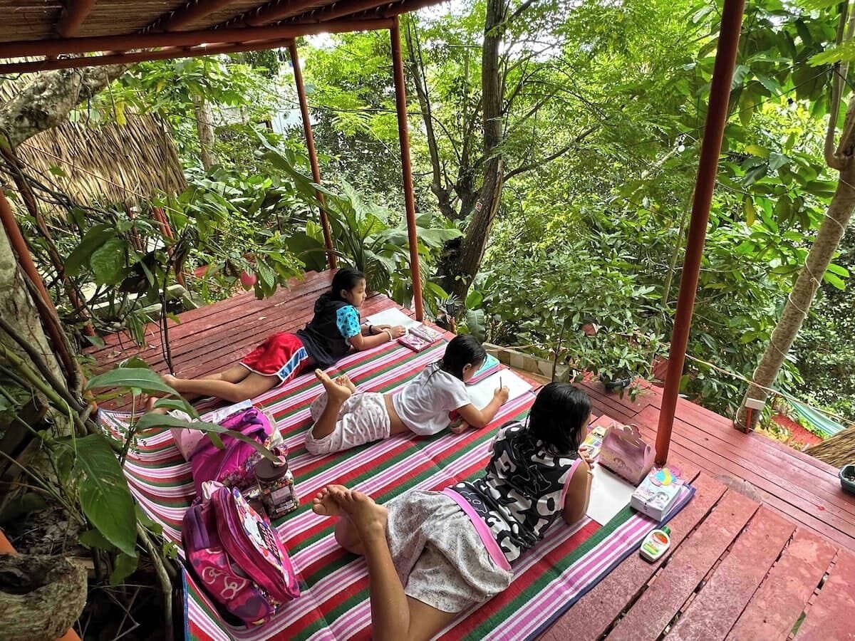 A wooden deck with a thatched roof, surrounded by lush greenery.