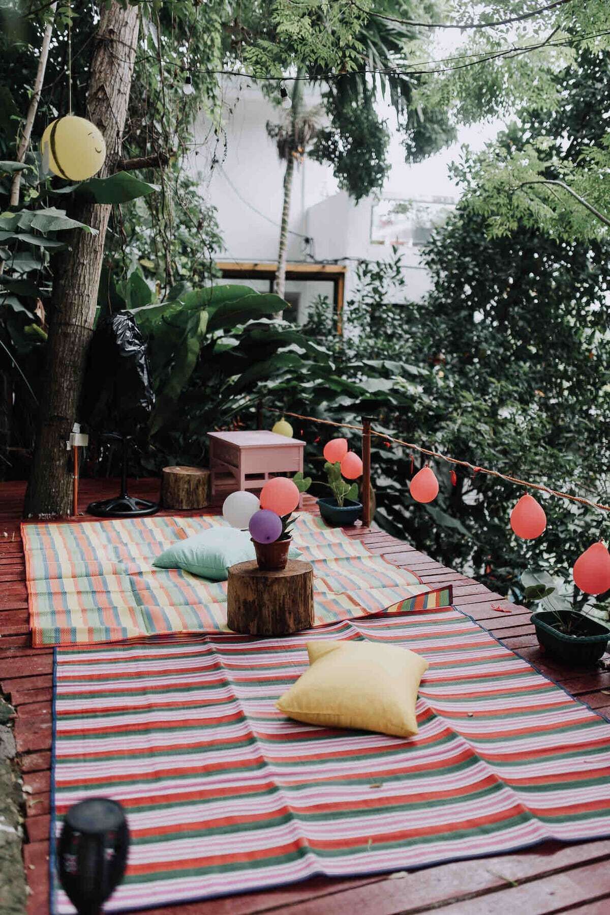 Una terraza de madera con esteras a rayas, un banco y una mesa con una planta en maceta.