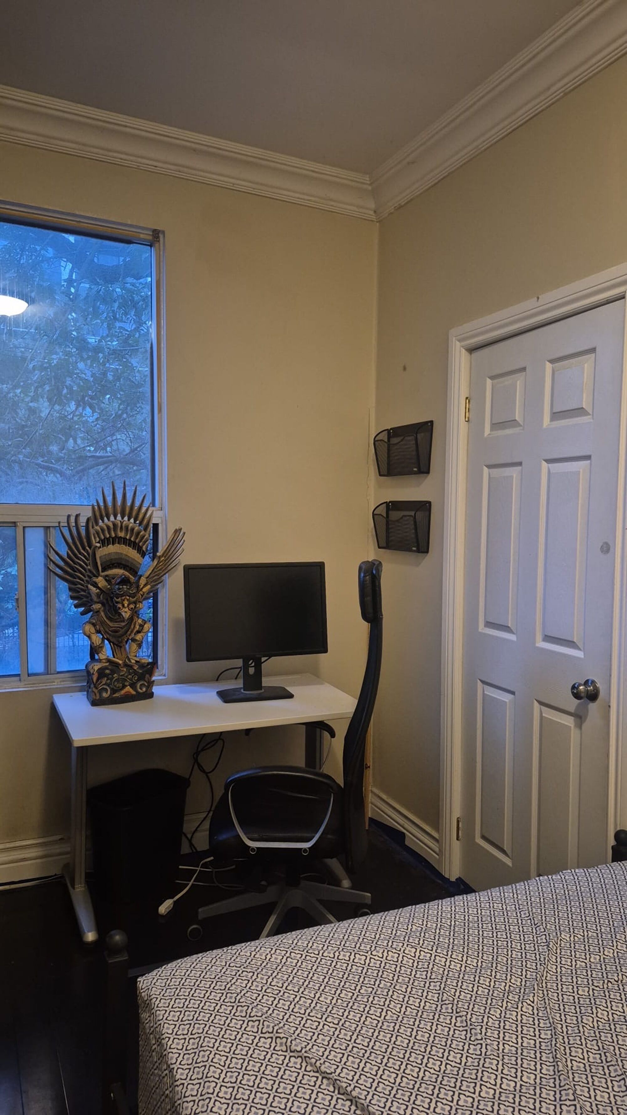 A bedroom with a bed, a desk with a computer, a chair, a window, and a door.