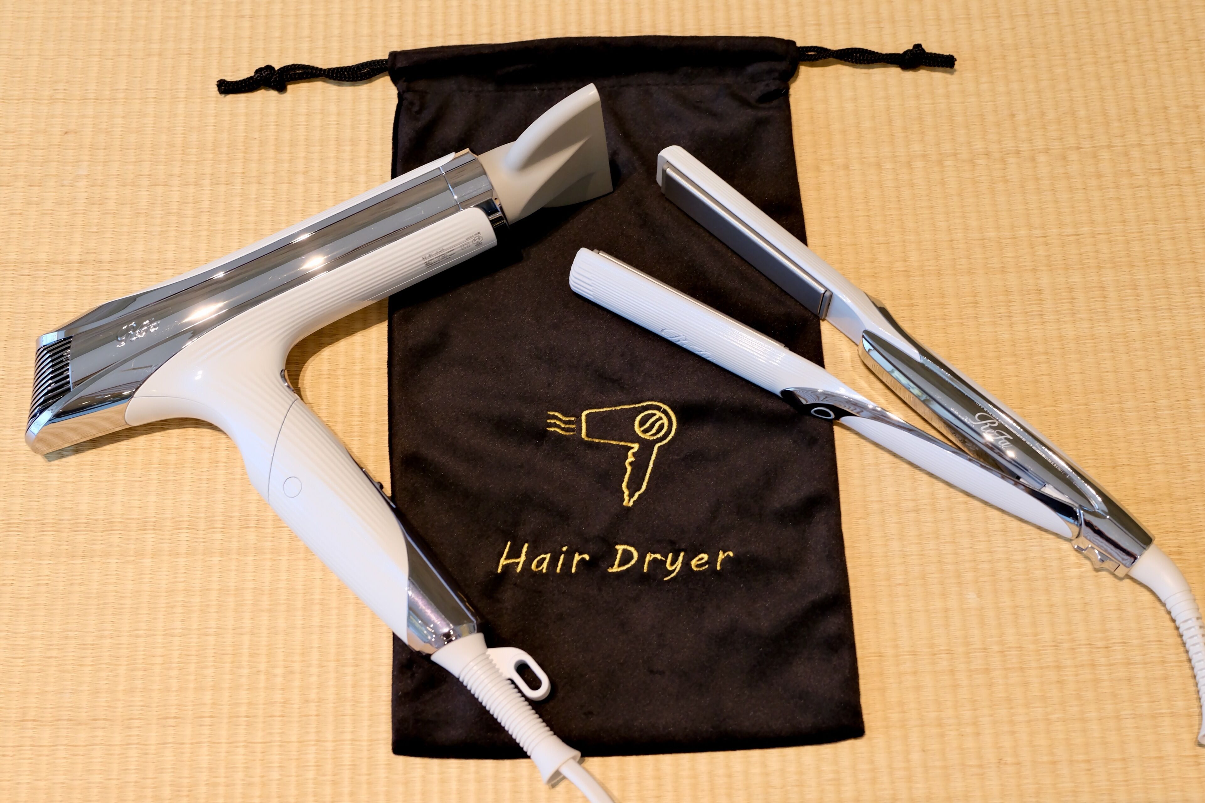 A hair dryer and a hair straightener on a brown cloth with the text 'Hair Dryer' and a hairdryer icon.