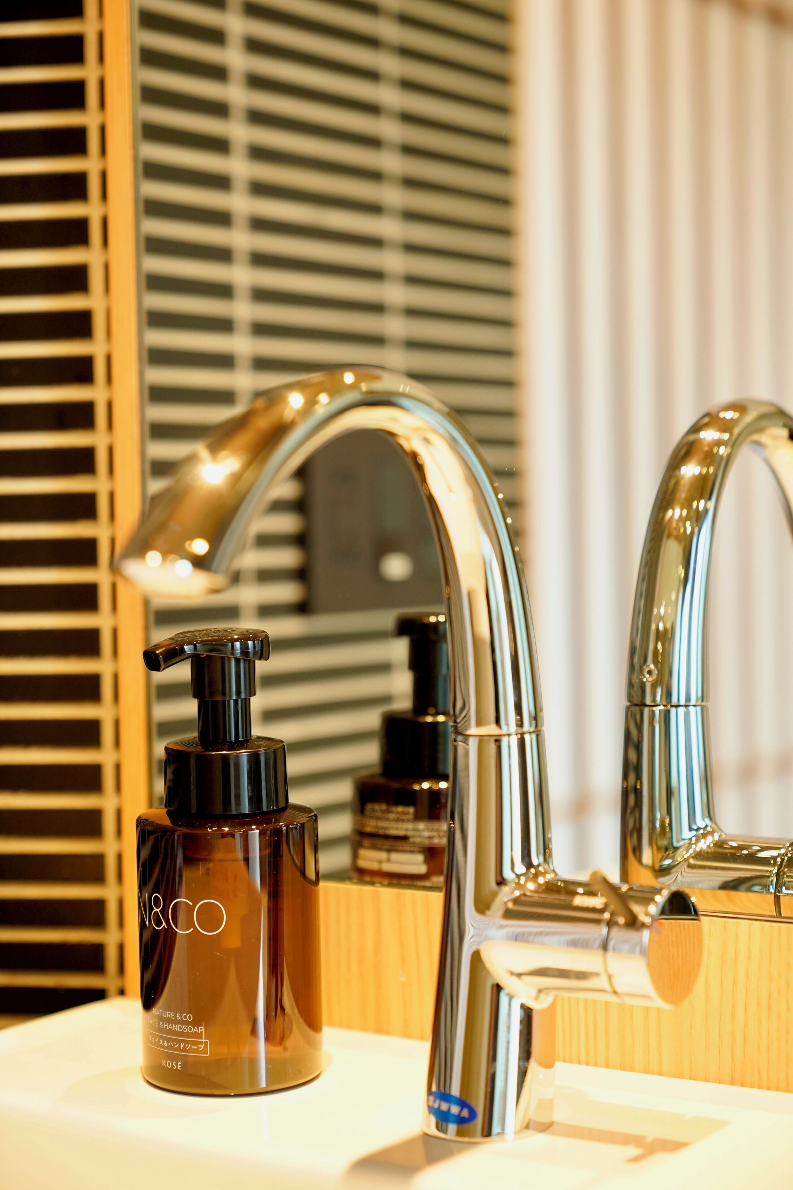 Een badkamer met een moderne kraan, een zeepdispenser en een spiegel die de ruimte weerspiegelt.