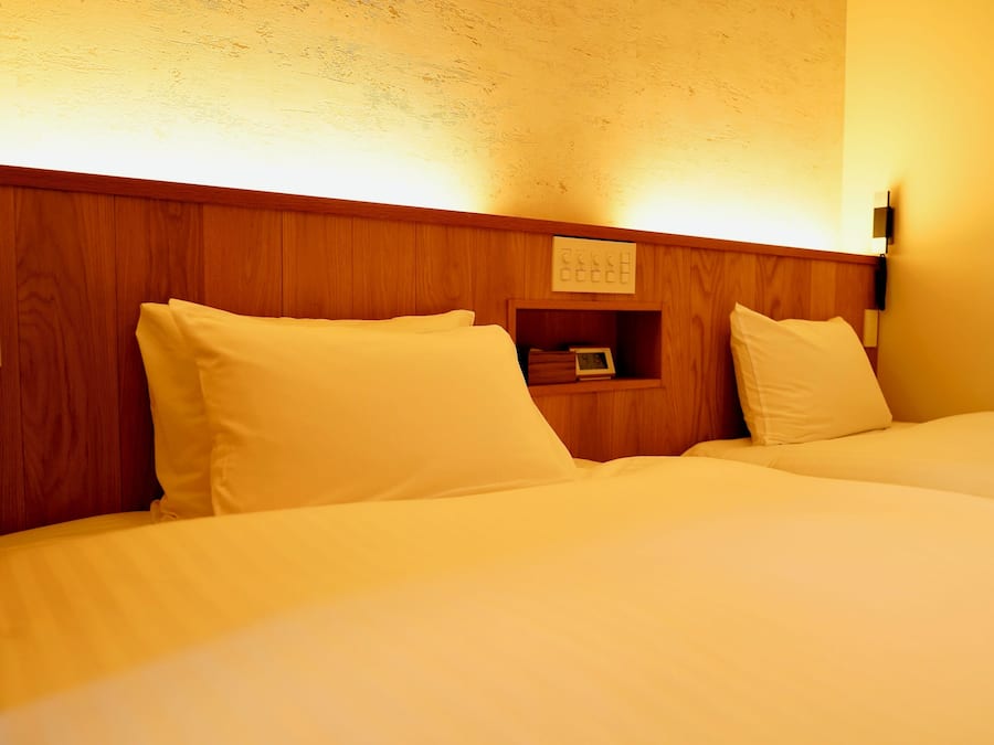 Een hotelkamer met twee bedden, een houten hoofdbord, nachtkastjes en een wandlamp.