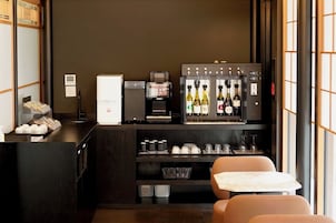 Habitación de hotel compacta con kitchenette, refrigerador, cafetera, enfriador de vino y una zona de estar con mesa y sillas.