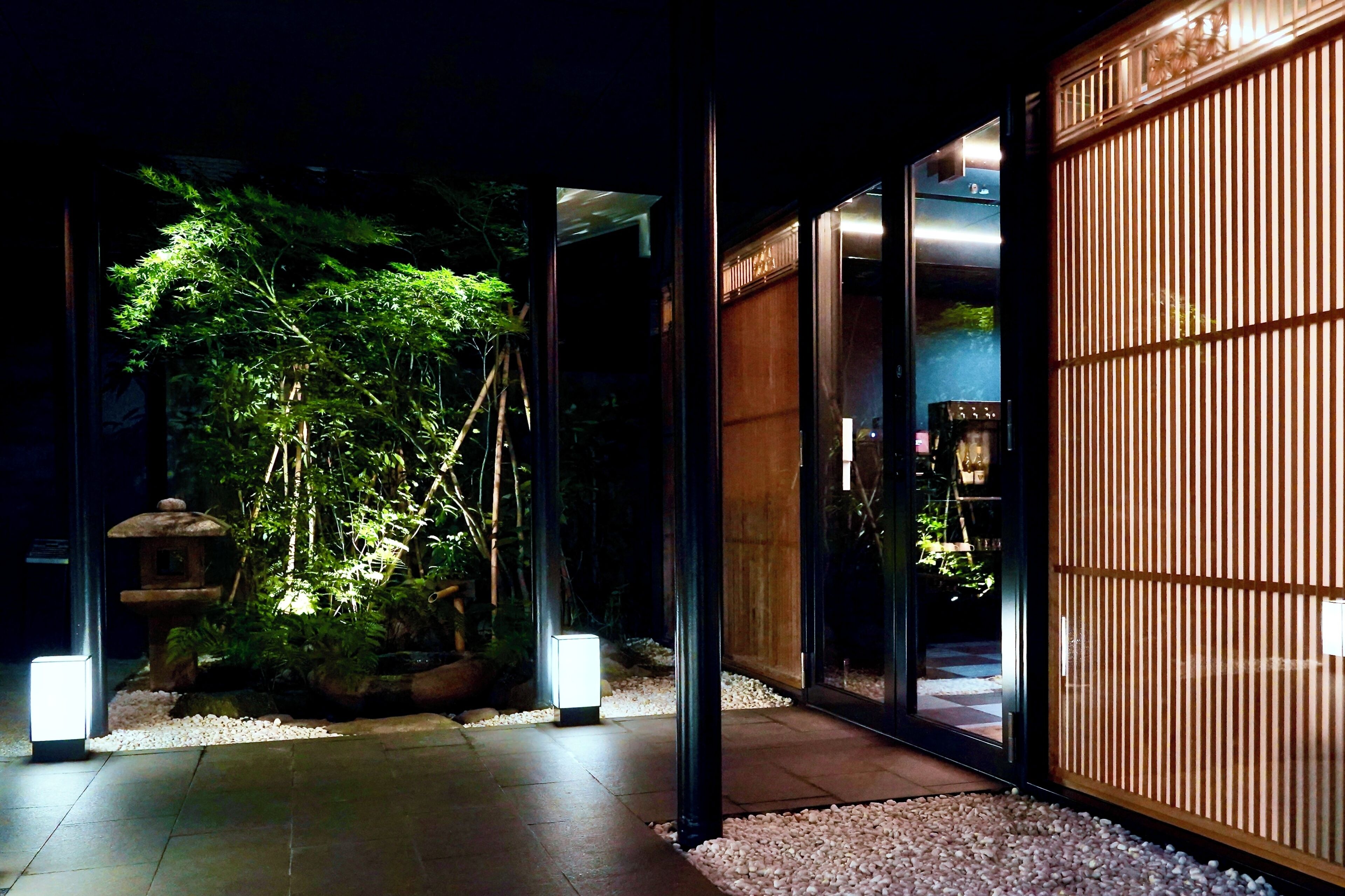 Um edifício moderno com entrada de vidro, um painel de bambu e um jardim bem iluminado.