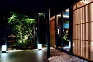 A modern building with a glass entrance, a bamboo screen, and a well-lit garden area.