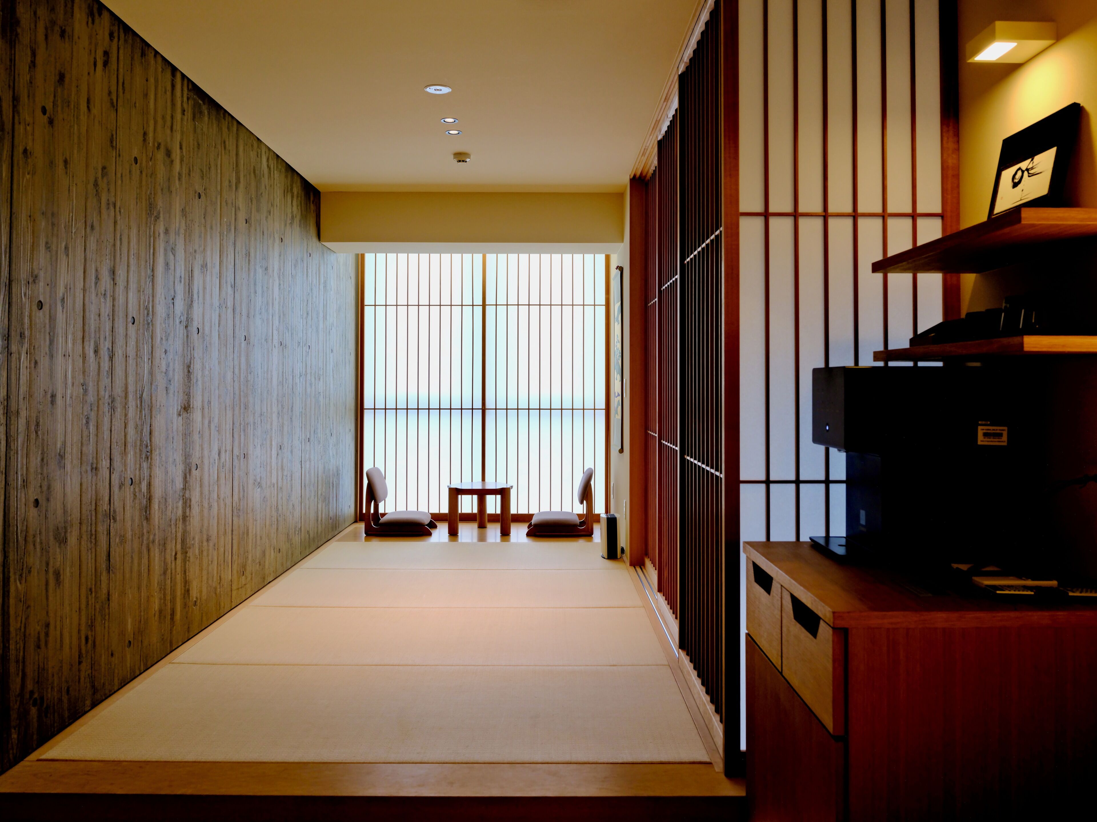 Habitació amb paviment de tatami, un escriptori de fusta baix, una televisió i una porta corredissa que dona a una vista.