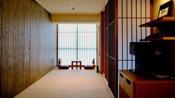 Habitació amb paviment de tatami, un escriptori de fusta baix, una televisió i una porta corredissa que dona a una vista.