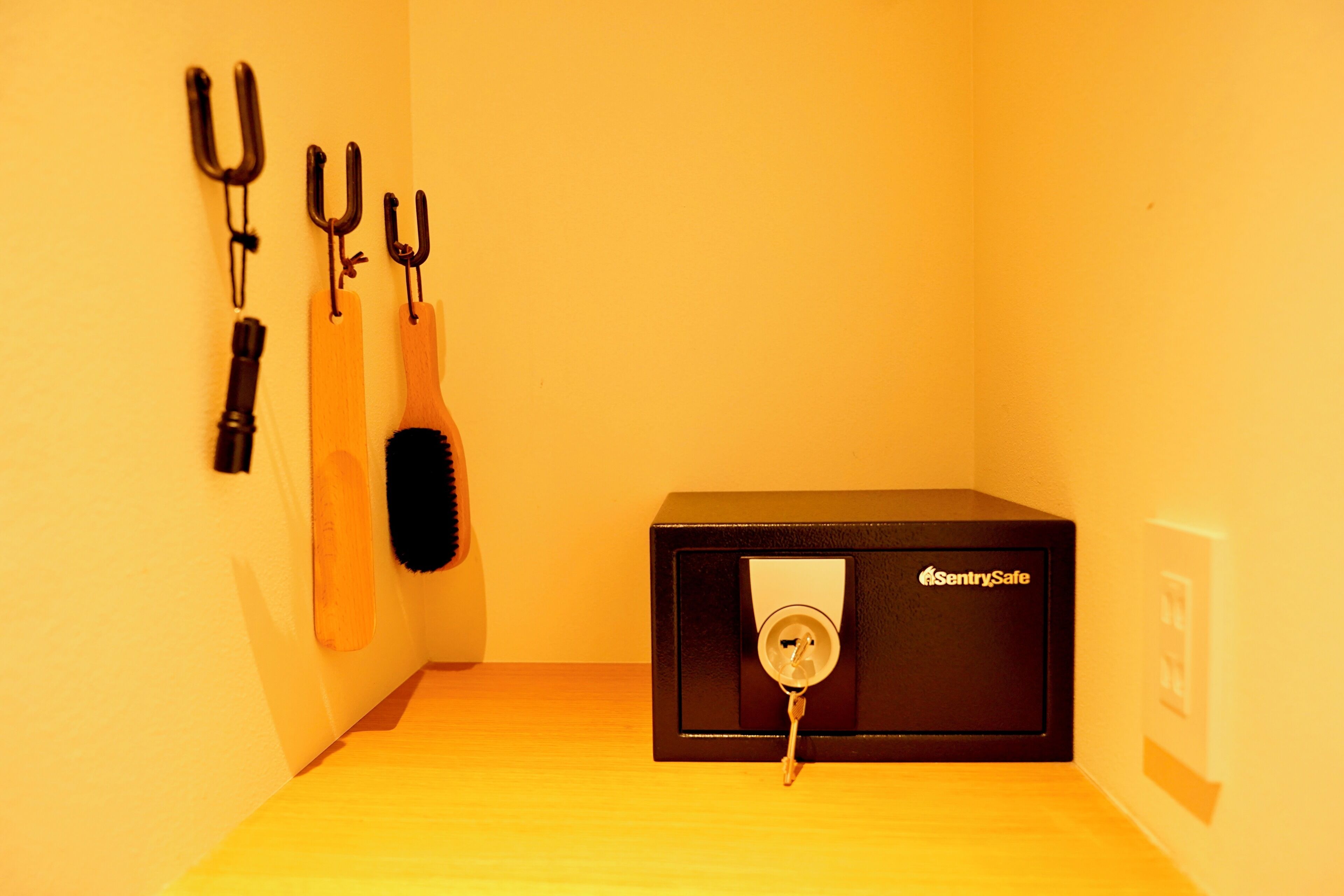 A room with a black safe, a wooden bench, and three hooks on the wall.