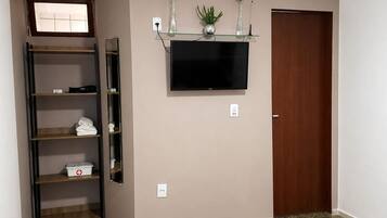A bedroom with a bed, a TV mounted on the wall, a wooden door, and a shelf with plants.