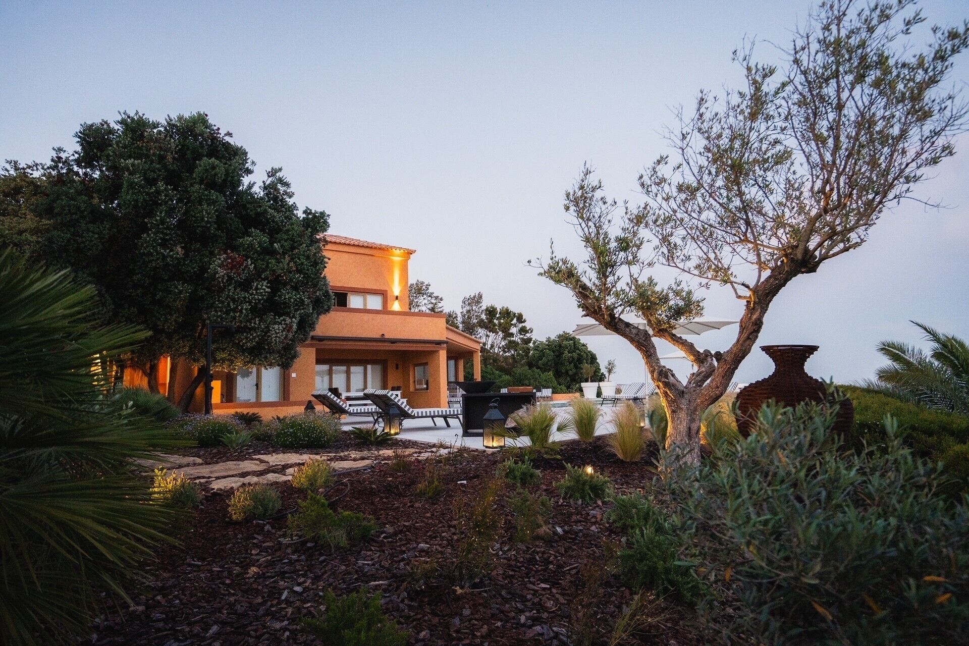 A two-story building with a pool, surrounded by trees and plants.