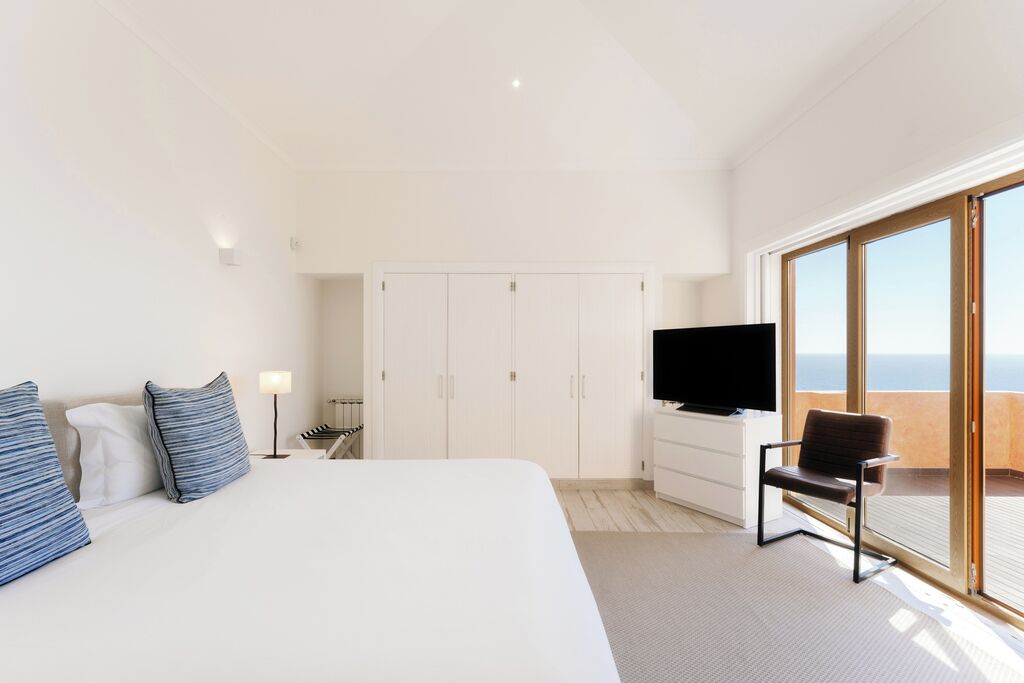 A bedroom with a large bed, a TV, a chair, and a wardrobe.