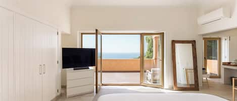 Quarto com cama, televisão, guarda-roupa, espelho e varanda com vista.