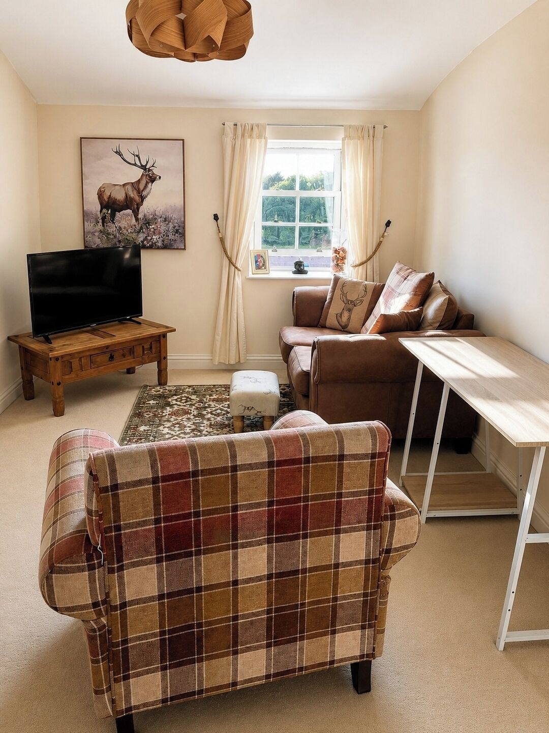 A living room with a sofa, a television on a wooden stand, a window with curtains, and a painting of a deer.