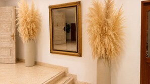 Un pasillo con un espejo, dos altos jarrones con plumas de pampa y una puerta de madera.