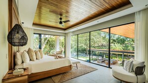 Een moderne slaapkamer met een groot bed, een bank, een plafondventilator en uitzicht op de omgeving.