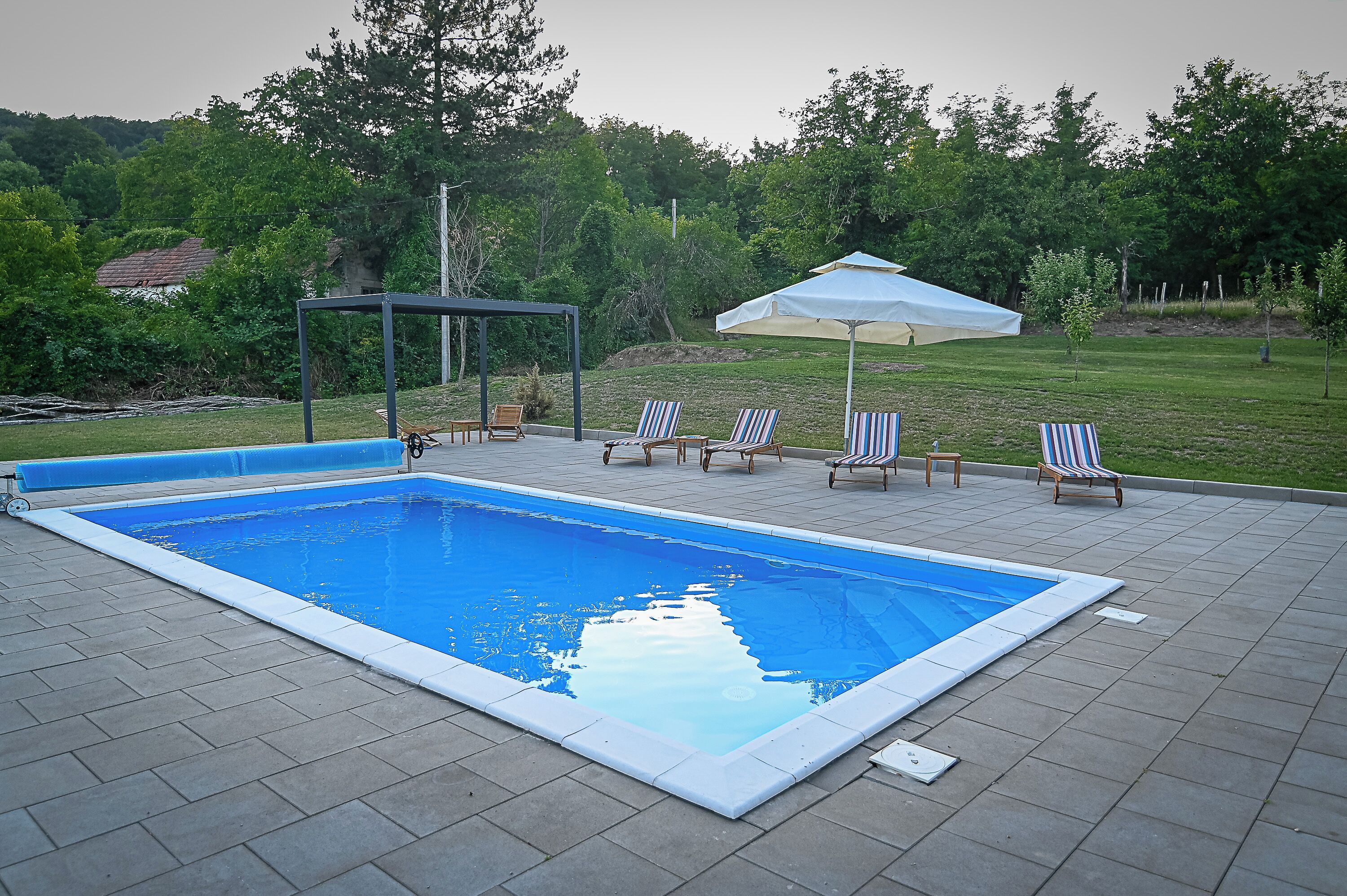 A rectangular swimming pool with a tiled deck, surrounded by lounge chairs and a covered seating area.