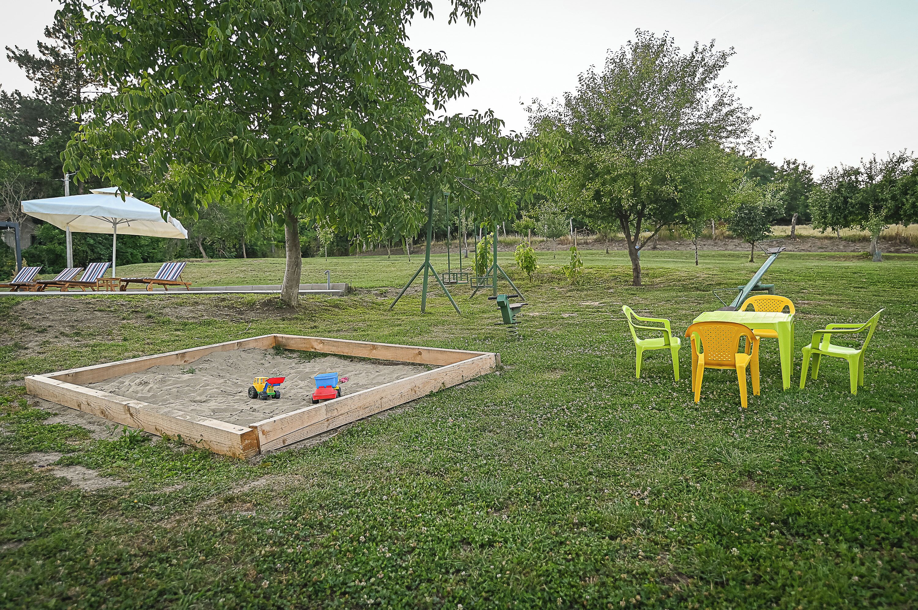 Una sabbiera con giochi, un tavolo con sedie e un'area salotto coperta.