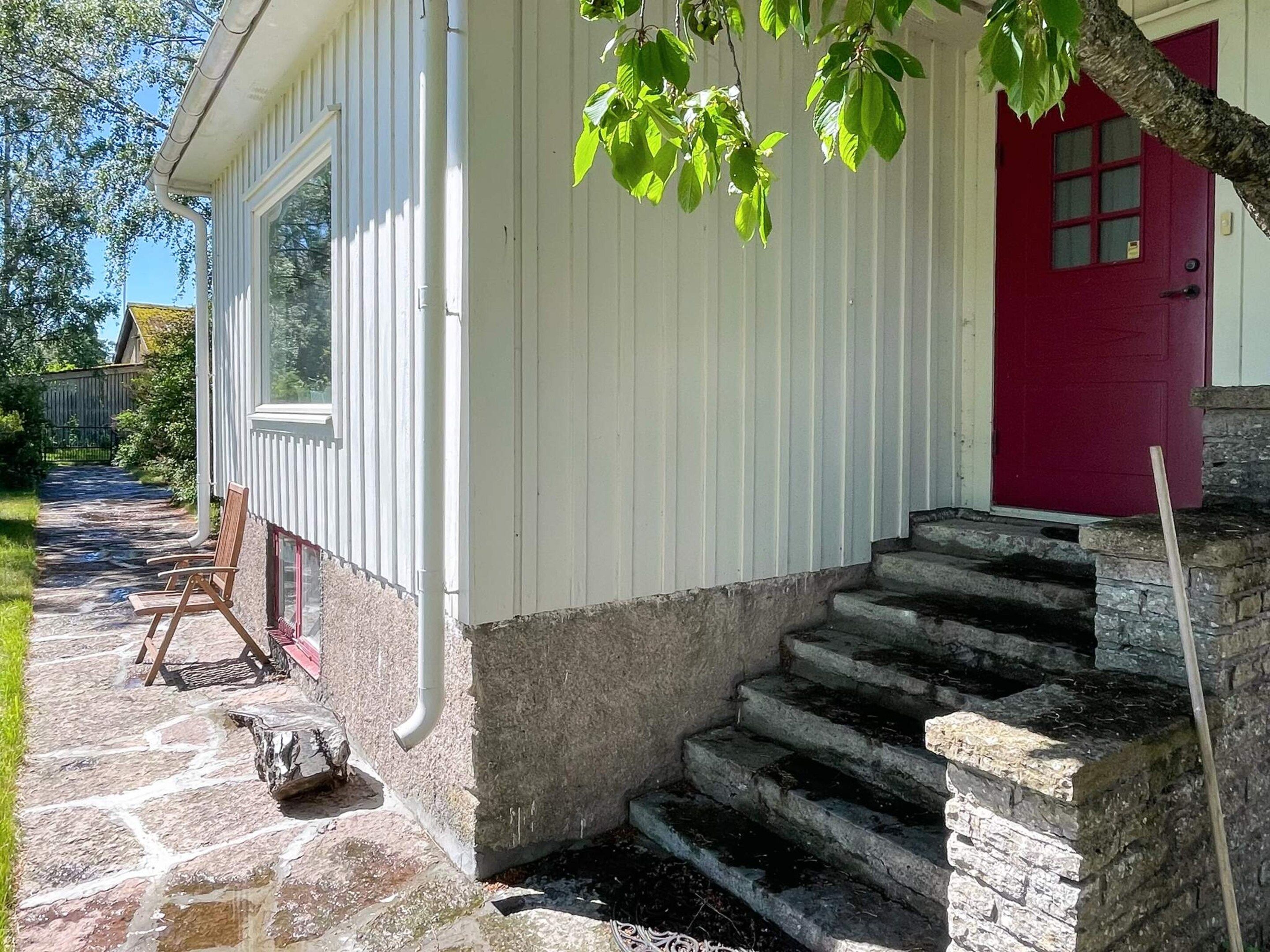 Una casa con puerta roja, escalones de piedra y pared exterior blanca.